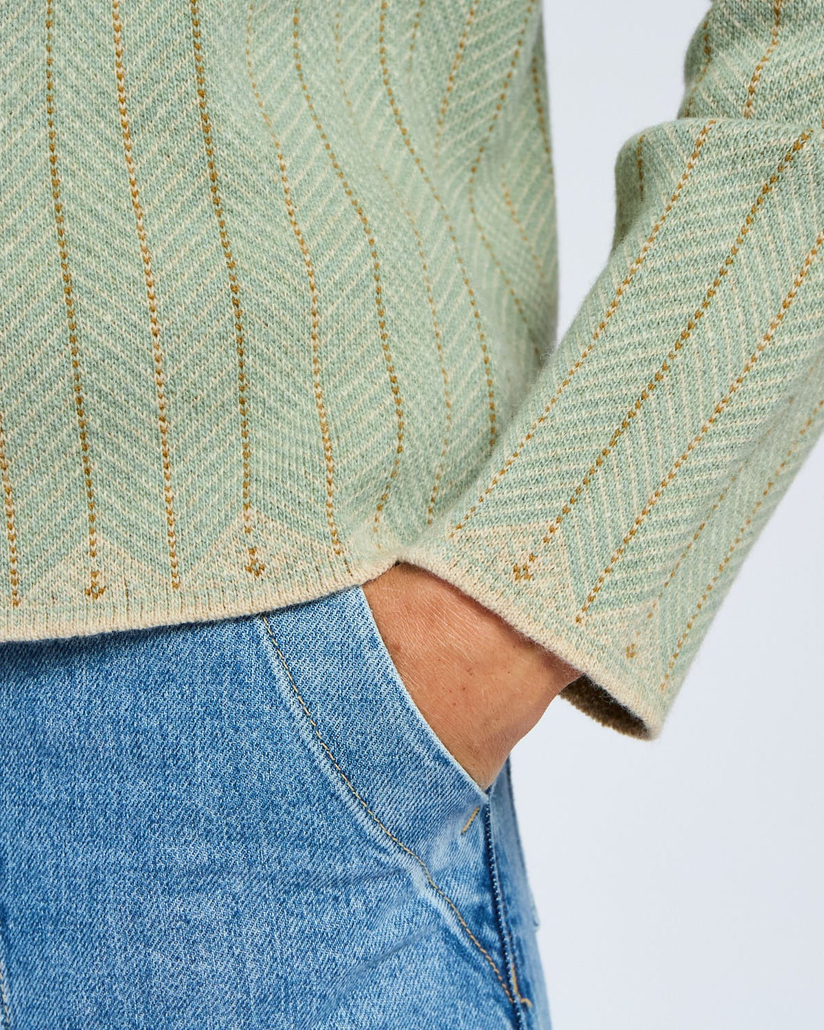 Green herringbone patterned sweater with blue jeans on a white background