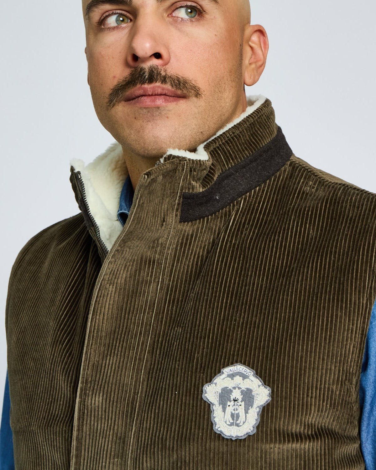 Man wearing a brown corduroy vest with a logo on a light gray background
