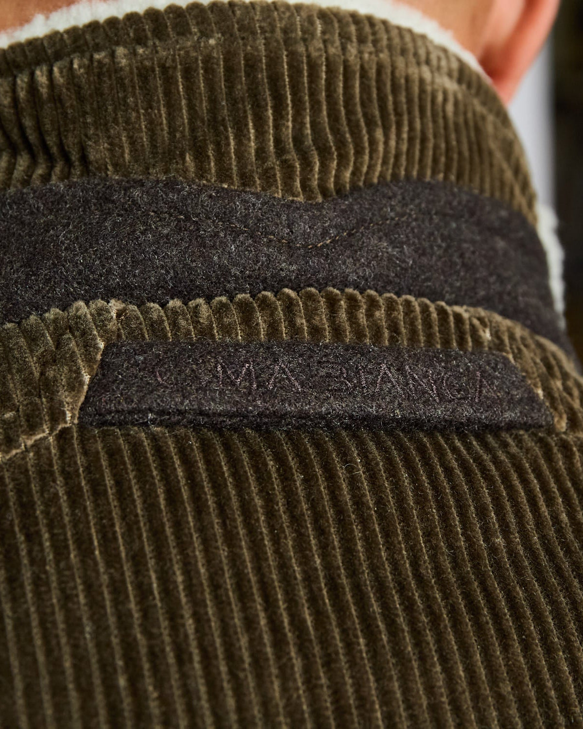 Close-up of a green corduroy jacket with a brand label on the chest.