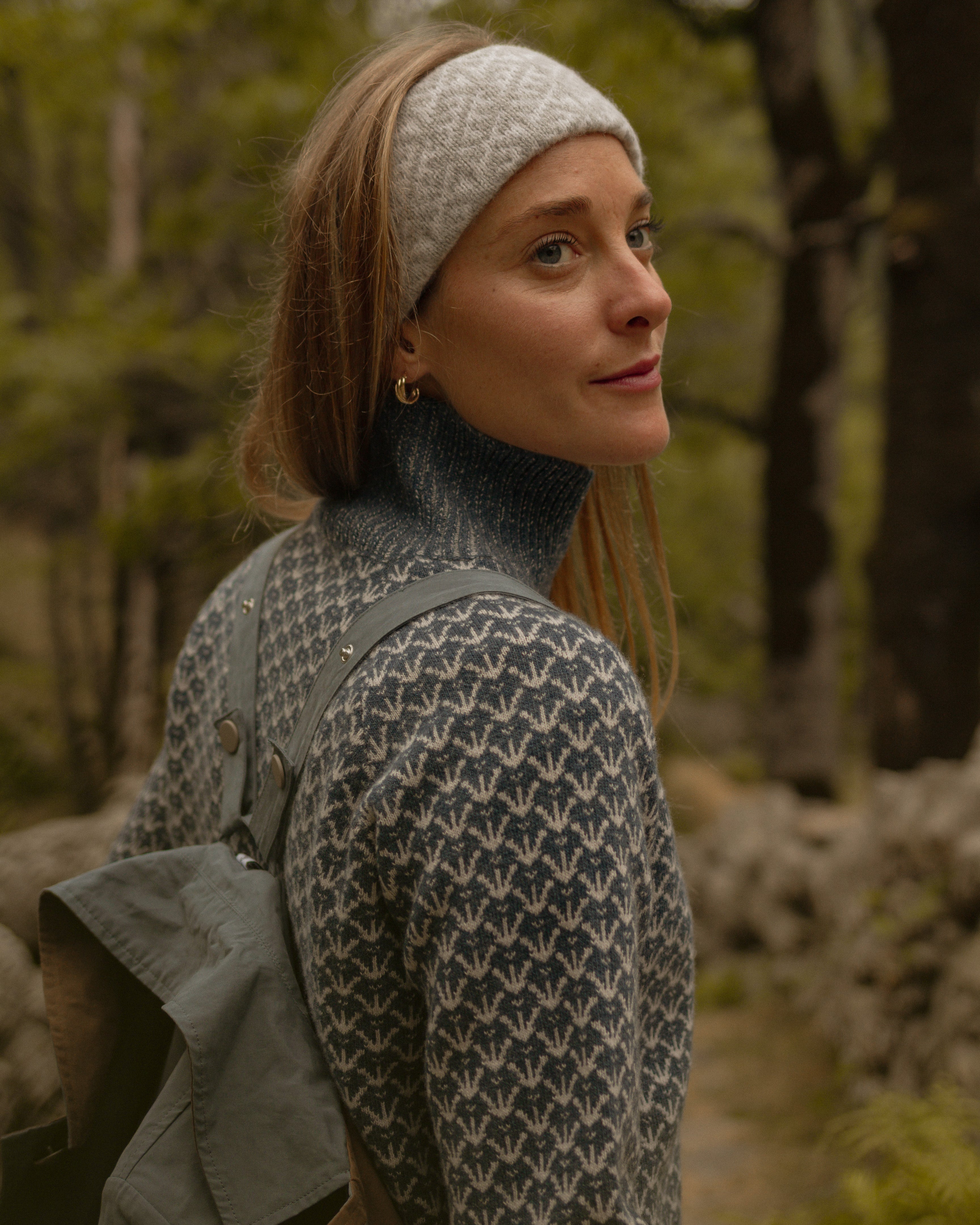 Woman wearing a patterned headband and sweater in a forest setting
