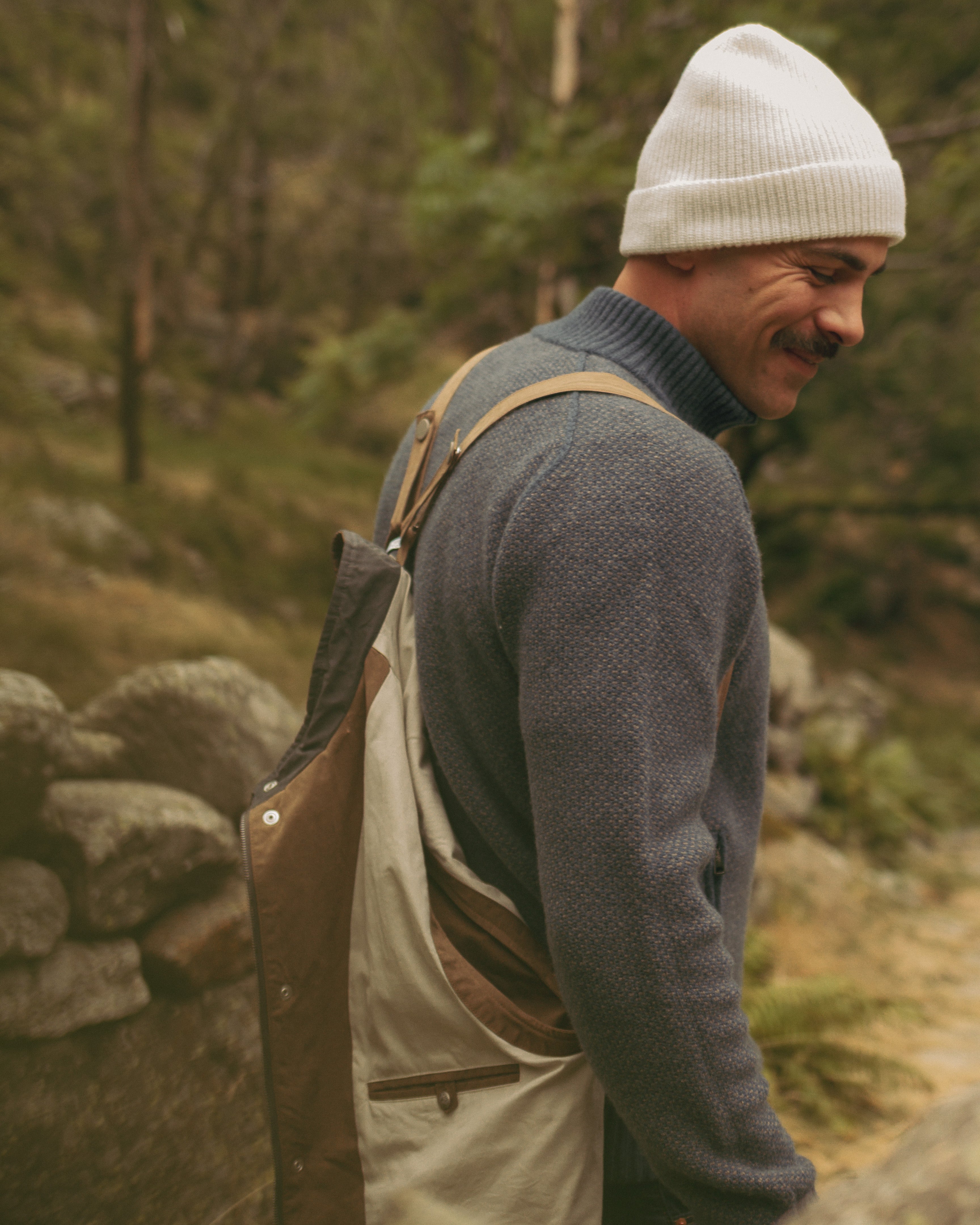Man wearing a white beanie and gray sweater with a backpack in a forest setting