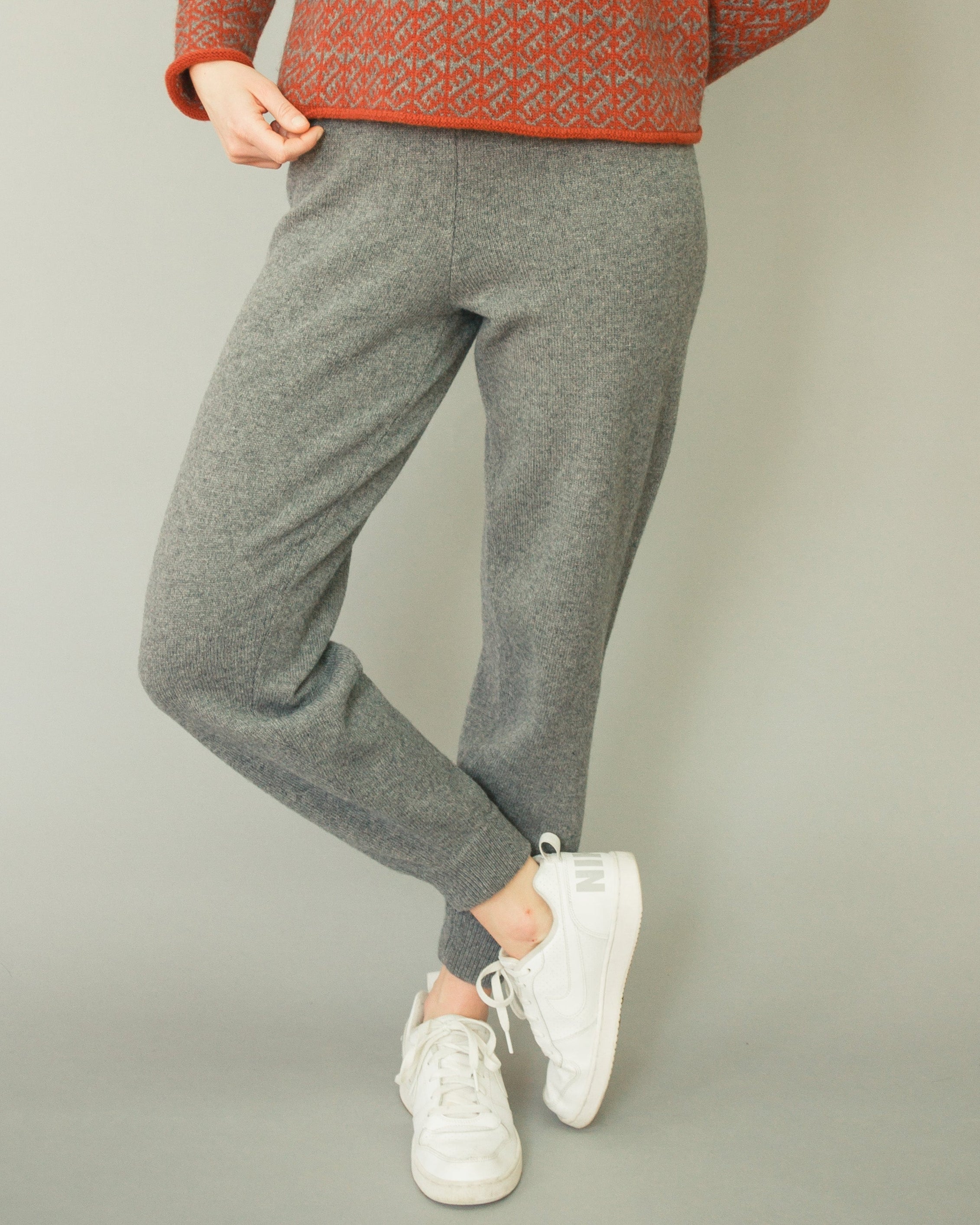 Woman wearing a red patterned sweater and gray pants on a plain background
